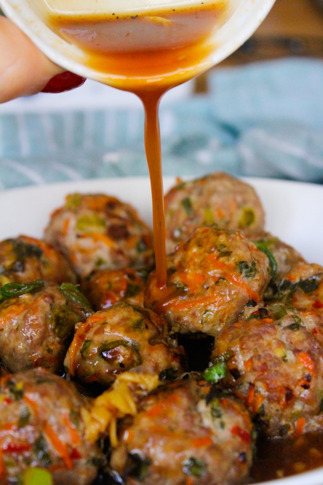 baked paleo thai meatballs stacked in a bowl with a chili sauce pouring over the top