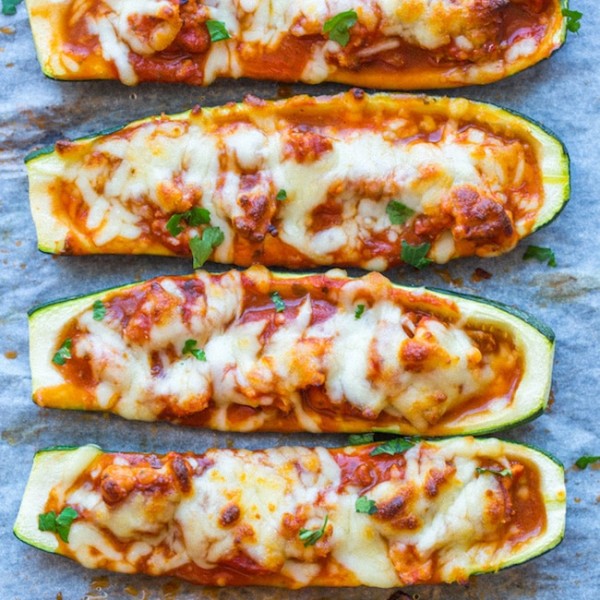 Zucchini Pizza Boats lined up on a baking sheet and topping with fresh herbs