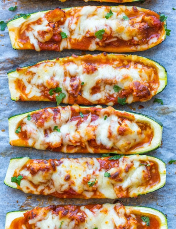 Zucchini Pizza Boats lined up on a baking sheet and topping with fresh herbs