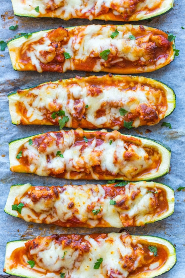 Zucchini Pizza Boats lined up on a baking sheet and topping with fresh herbs