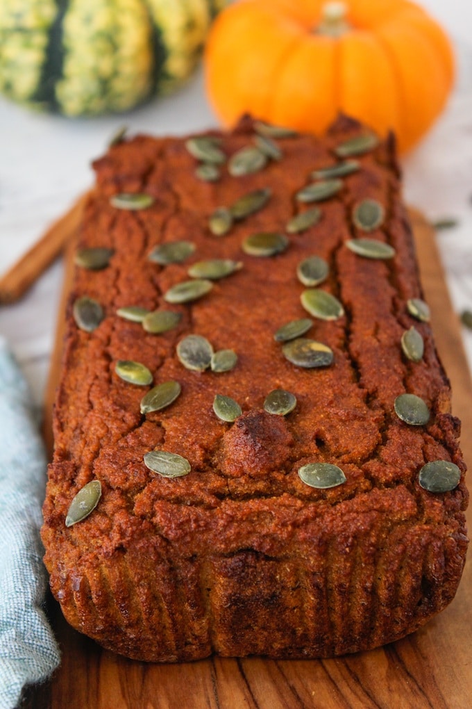 Paleo Pumpkin Bread topped with pepitas with a small baby pumpkin in the background