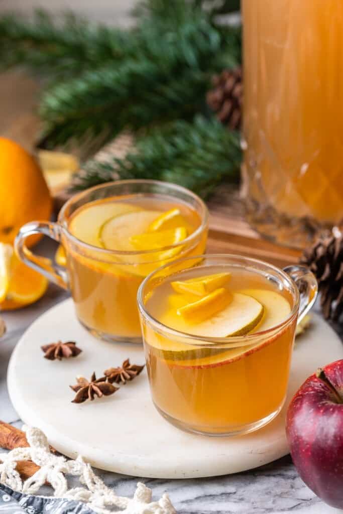 a couple of mugs full of mulled apple pear cider with whole star anise and an apple next to them