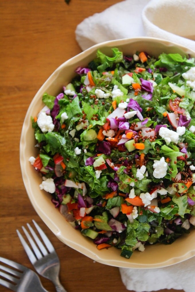 a large bowl filled with a lettuce, quinoa, radish, carrot and feta salad