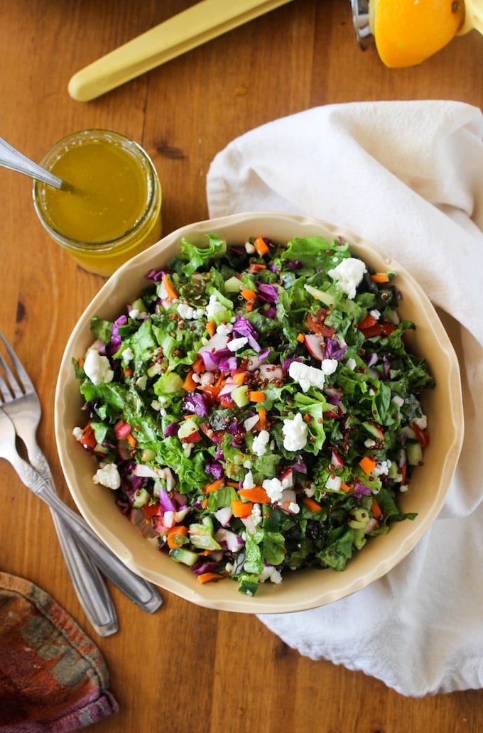 a large bowl filled with a lettuce, quinoa, radish and carrot salad with an orange vinaigrette on the side