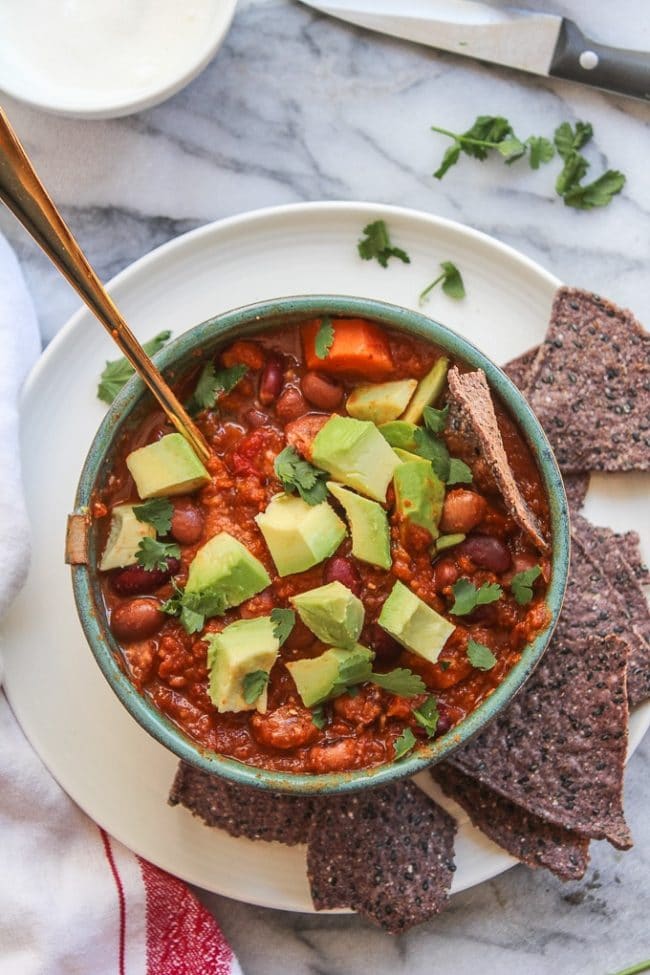 Chunky Vegetarian Chili in a bowl topped with avocado and blue tortilla chips 