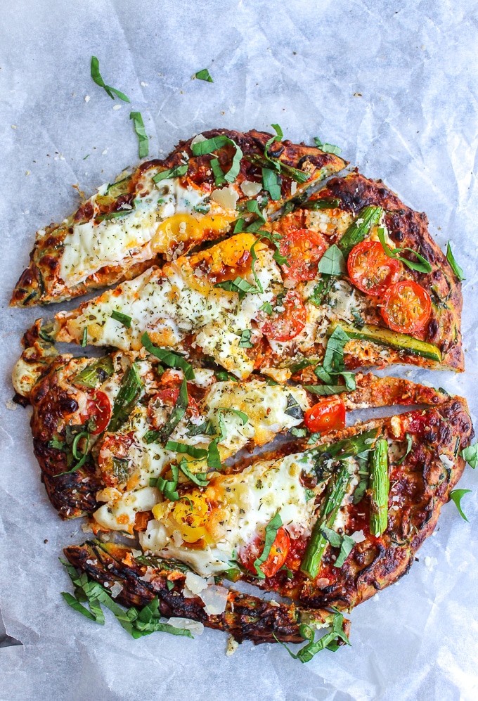 Zucchini Crusted Breakfast Pizza topped with sliced asparagus, cherry tomatoes, eggs, and a sprinkling of parmesan cheese.