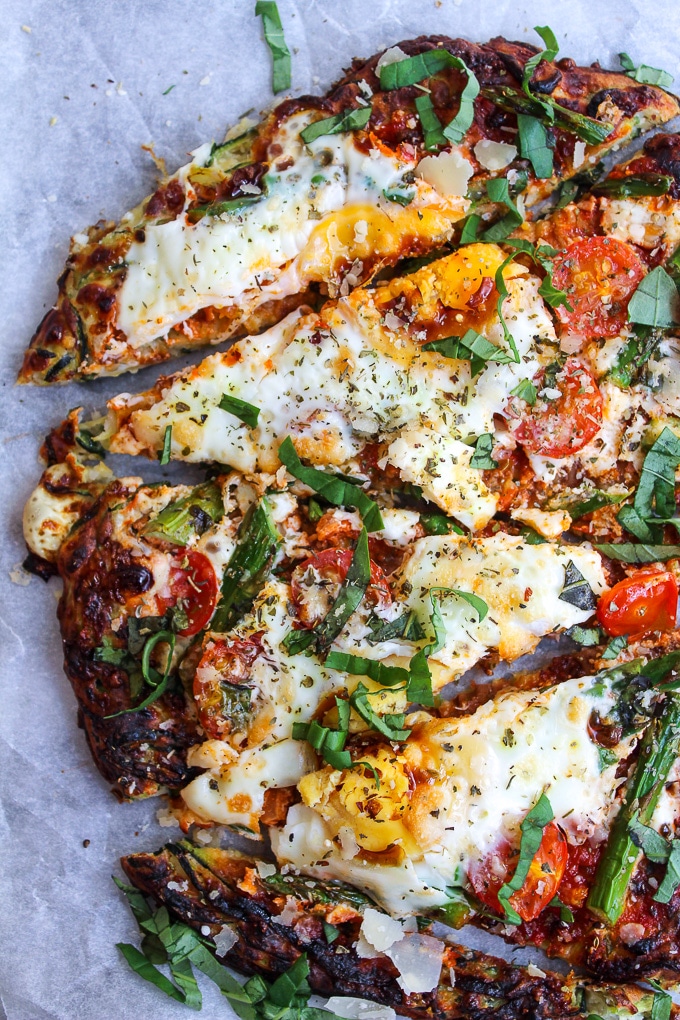 Zucchini Crusted Breakfast Pizza topped with sliced asparagus, cherry tomatoes, eggs, and a sprinkling of parmesan cheese.