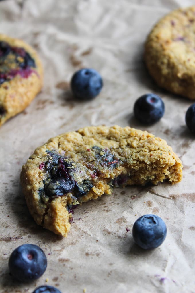 Oatmeal Blueberry Cookies on baking paper with fresh blueberries surrounded by a cookie with a bite taken out