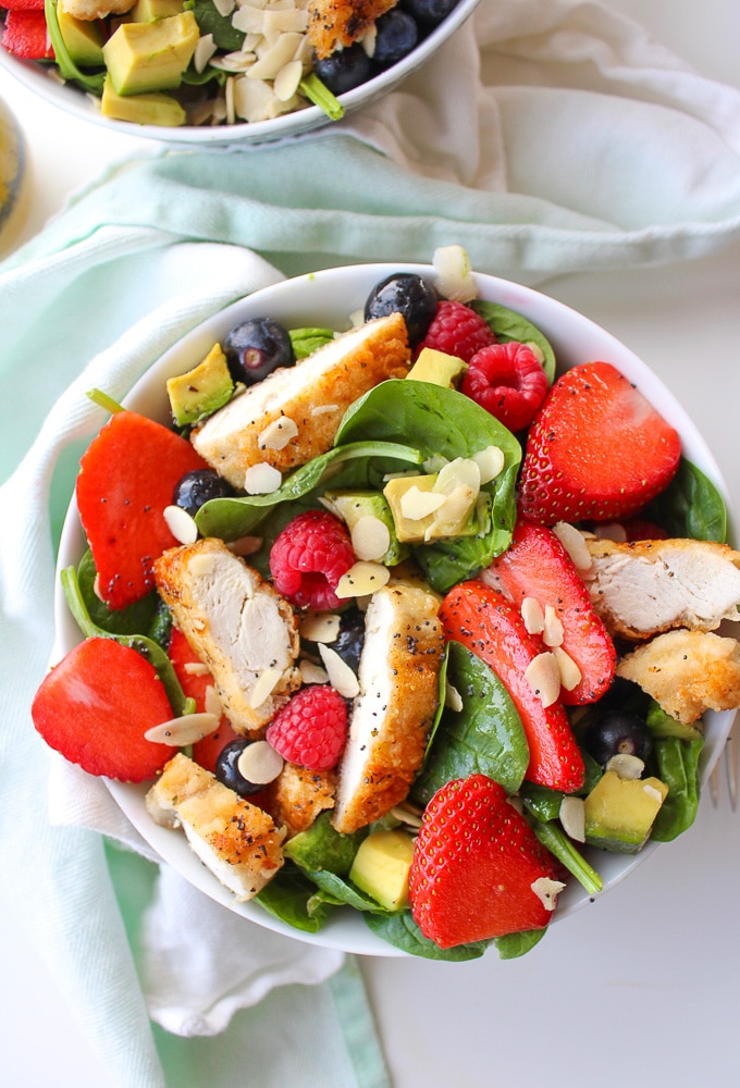 Easy mixed berry spinach salad with avocado, pan fried chicken,and flaked almonds dressed in a simple, honey poppy seed dressing!