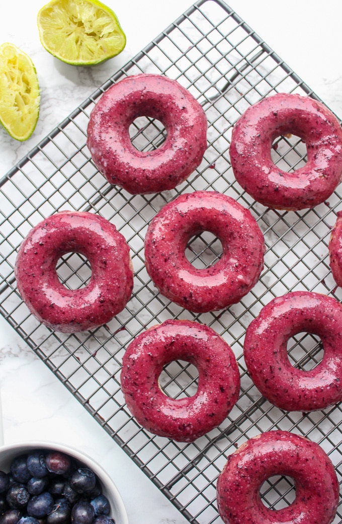 seven baked vegan donuts on a cooling rack covered in a blueberry lime glaze