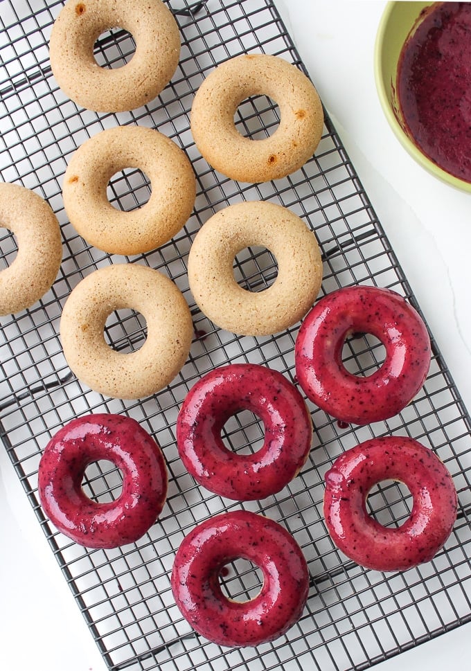 10 baked vegan donuts on a cooling rack - five donuts covered in a with a blueberry glaze and 6 donuts unglazed