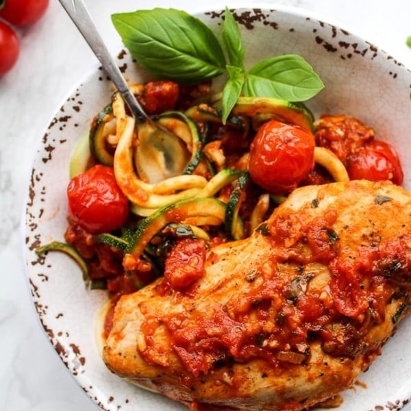 Tomato Basil Garlic Chicken over zucchini noodles in a bowl garnished with basil