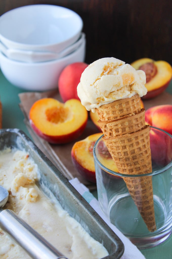 a waffle cone with coconut peach ice cream in a cup next to a container of the homemade ice cream 