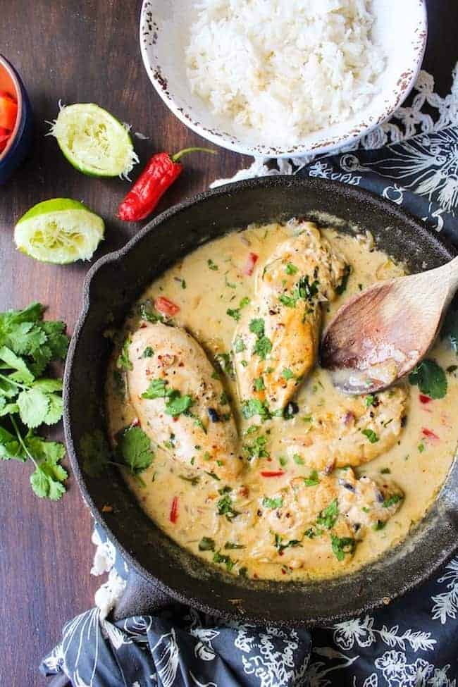 Coconut Lime Chicken in a cast iron skillet with a spoon surrounded by limes and cilantro 