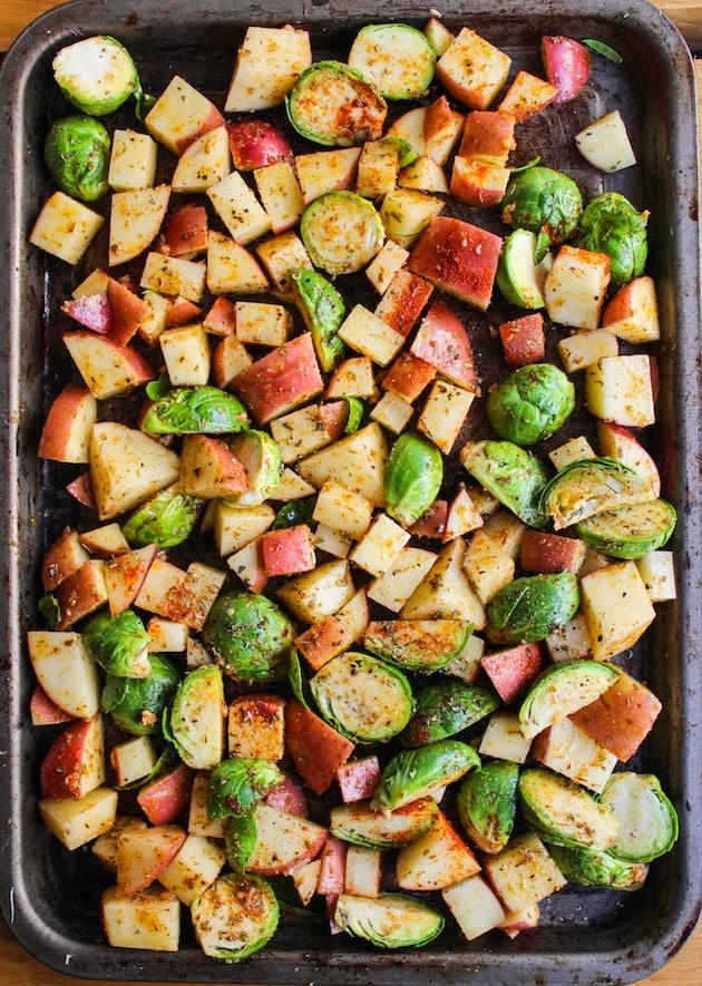 a baking sheet with uncooked, seasoned potatoes and sprouts