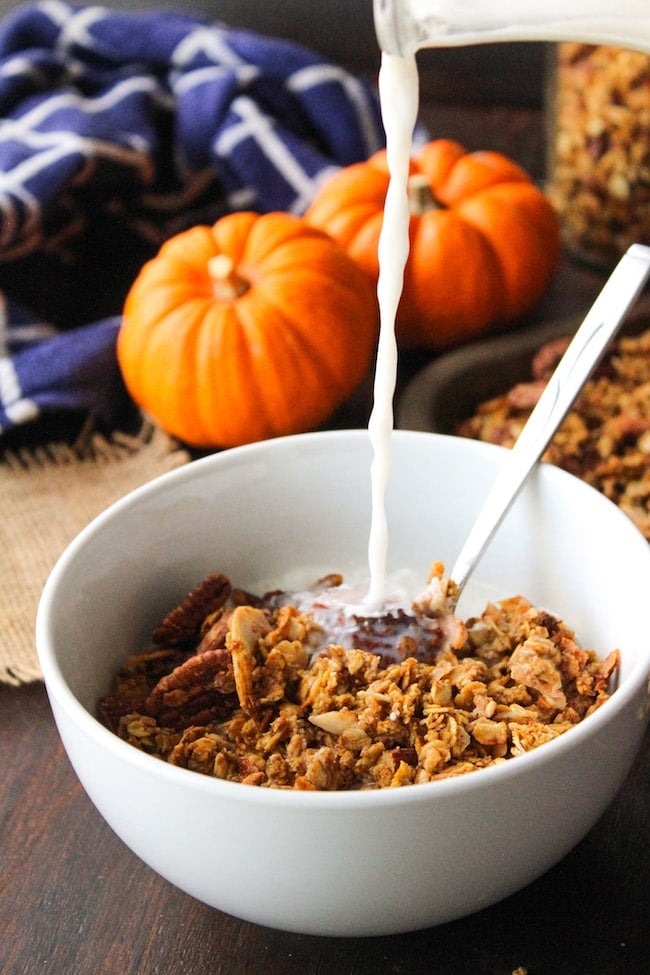 Pumpkin Spice Granola in a cereal bowl with almond milk pouring into the bowl