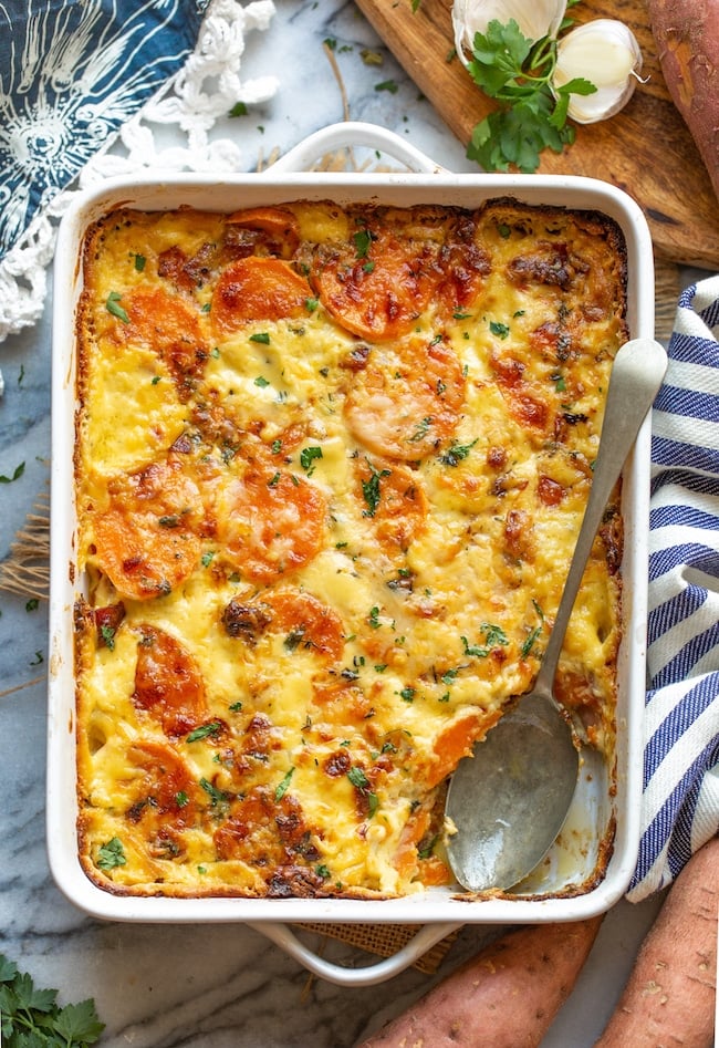 scalloped sweet potatoes in a baking dish with a serving spoon