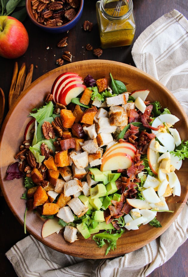 Loaded Autumn Cobb Salad in a bowl surrounded by pecans and apples