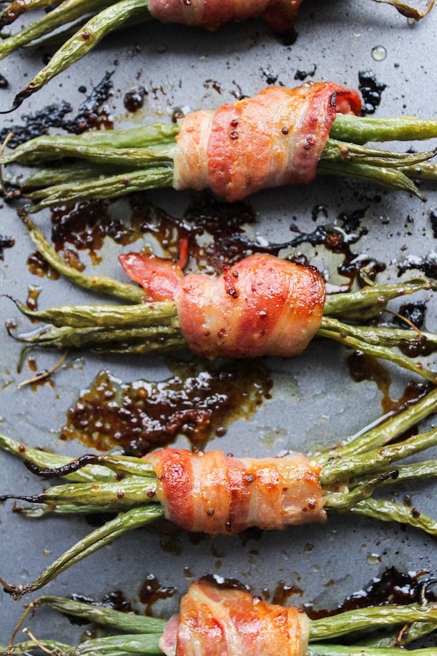 baked green beans wrapped in bacon and coated in a honey mustard sauce on a baking sheet 