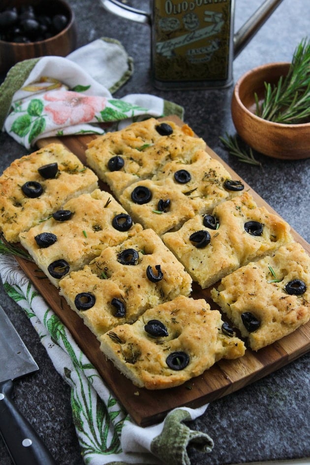 Gluten Free Focaccia Flatbread topped with sliced black olives and fresh rosemary. Made Vegan with aquafaba instead of eggs