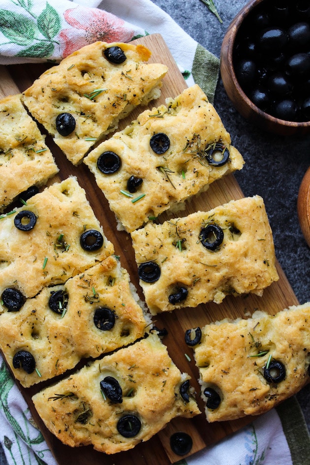 Gluten Free Focaccia Flatbread topped with sliced black olives and fresh rosemary. Made Vegan with aquafaba instead of eggs