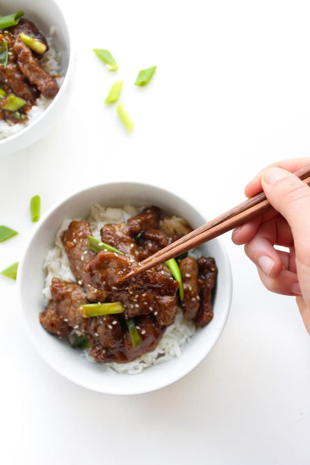 Paleo Mongolian Beef in a bowl topped with spring onions and chop sticks pick a piece up