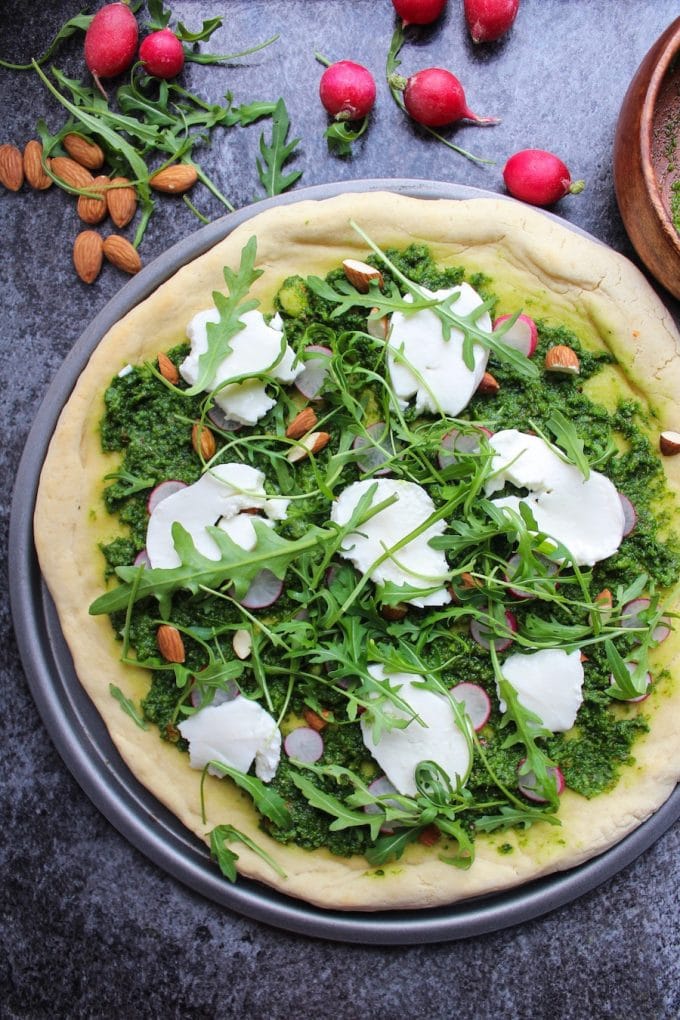 Super Green Kale Pesto Pizza topped with arugula, sliced radishes, chopped almonds and dollops of mozzarella. Gluten Free + Vegetarian 