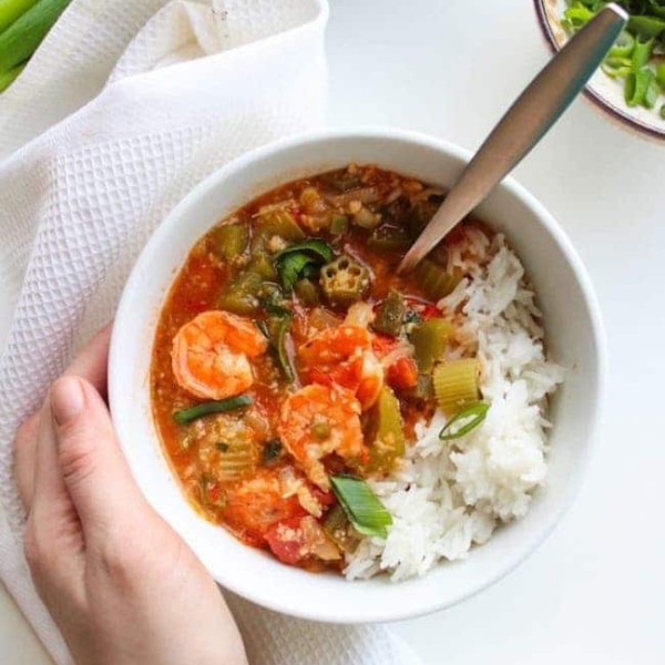 One pot Fast Seafood Gumbo in a soup bowl with rice and a hand holding the bowl