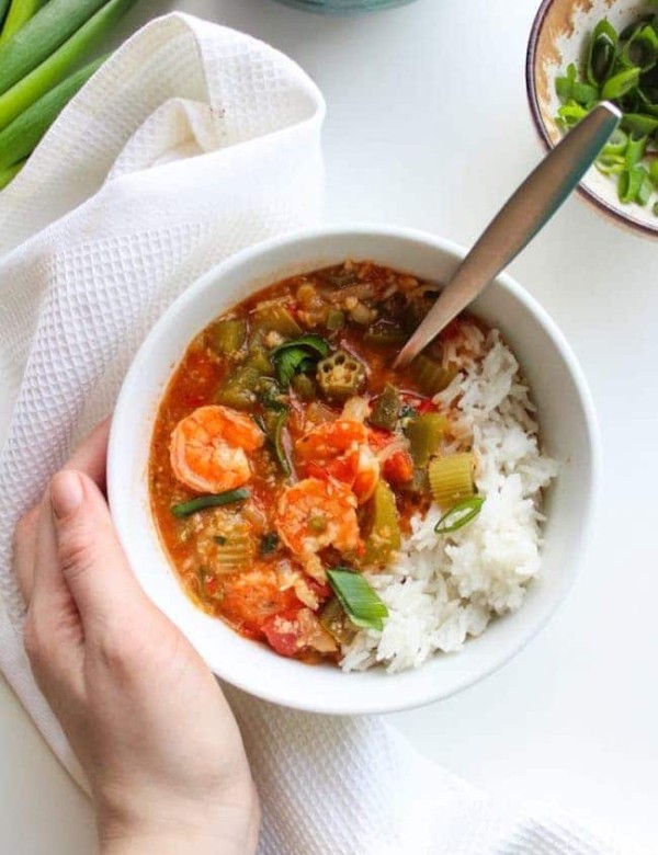 One pot Fast Seafood Gumbo in a soup bowl with rice and a hand holding the bowl
