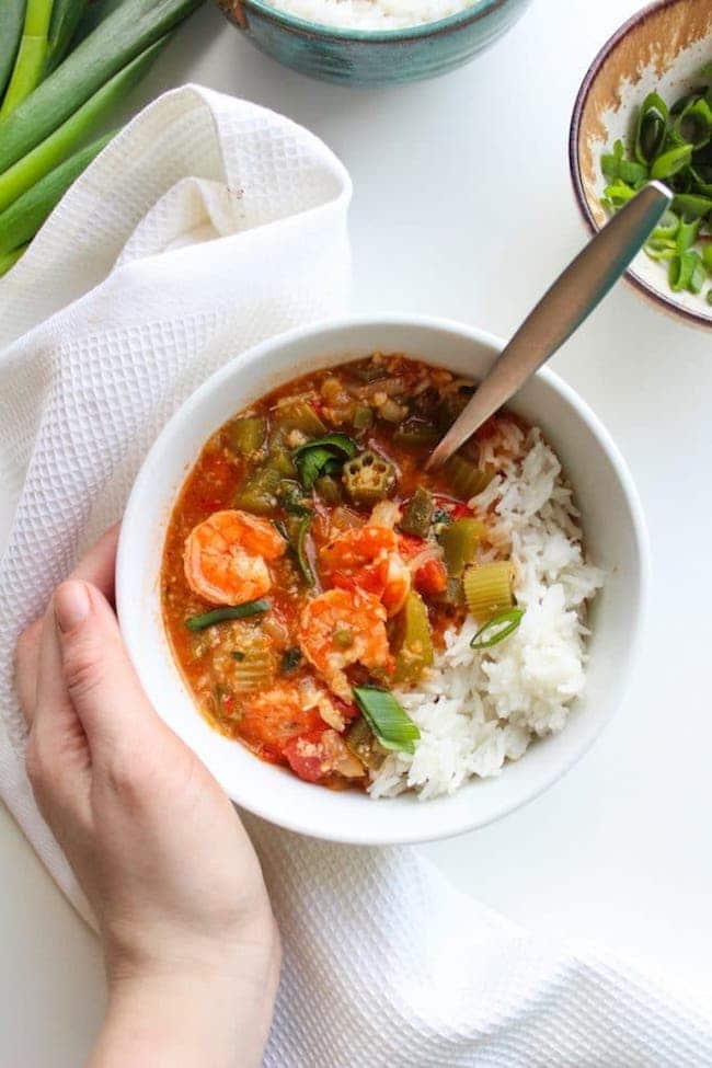 One pot Fast Seafood Gumbo in a soup bowl with rice and a hand holding the bowl 