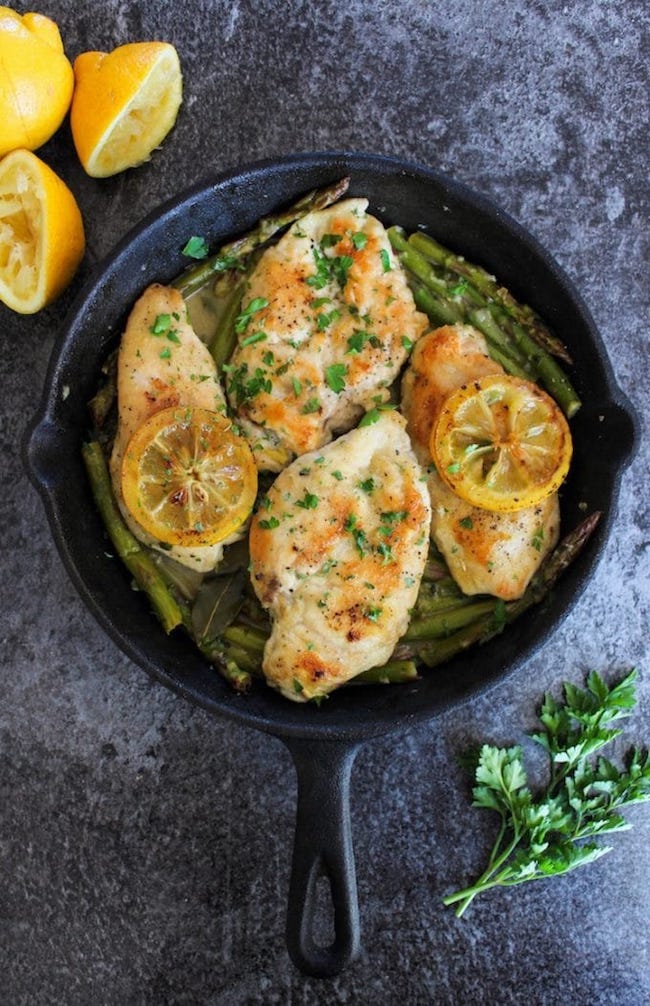 One Pan Lemon Chicken in a cast iron skillet topped with grilled lemons and parsley 