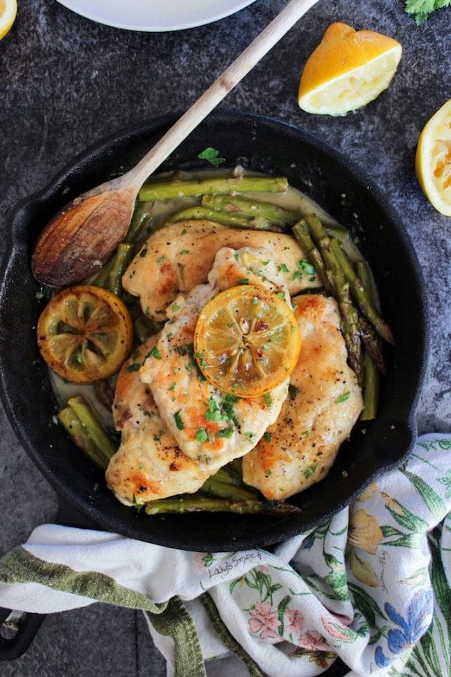 One Pan Lemon Chicken in a cast iron skillet topped with grilled lemons and parsley