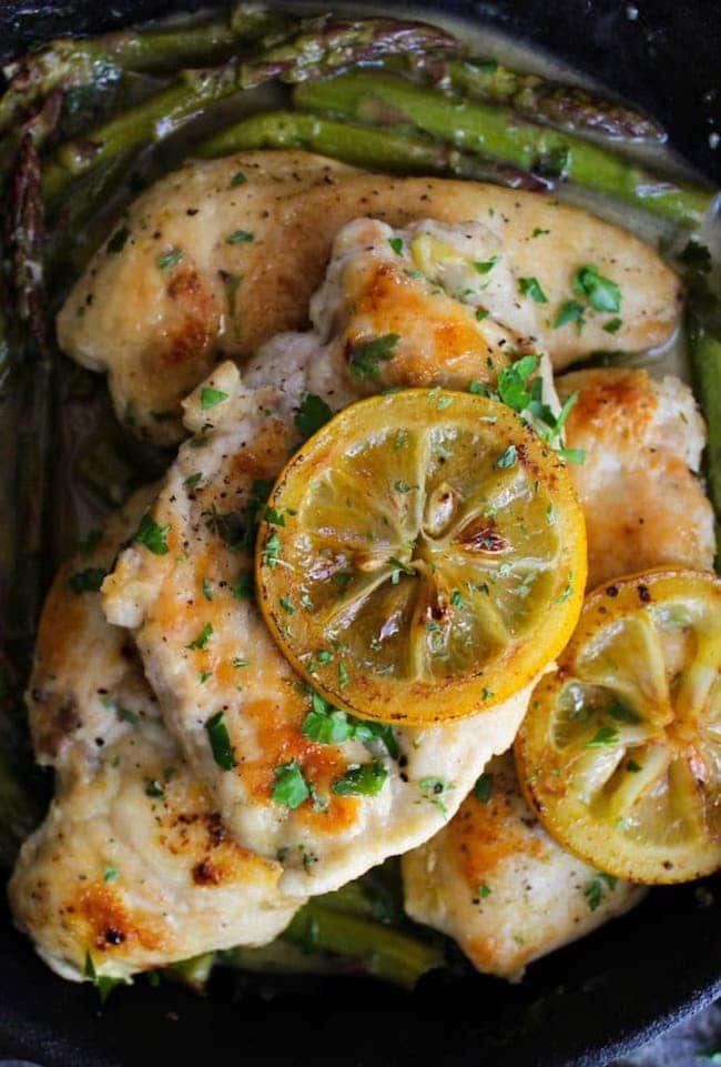 up close One Pan Lemon Chicken in a cast iron skillet topped with grilled lemons and parsley 