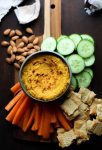 Roasted Carrot Hummus on a serving board with chips and sliced veggies
