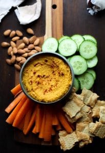Roasted Carrot Hummus on a serving board with chips and sliced veggies
