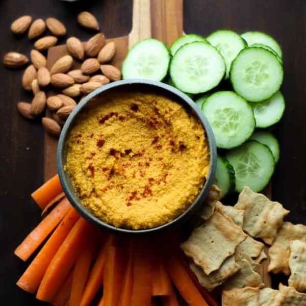 Roasted Carrot Hummus on a serving board with chips and sliced veggies