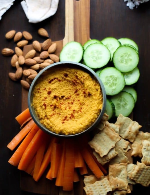 Roasted Carrot Hummus on a serving board with chips and sliced veggies