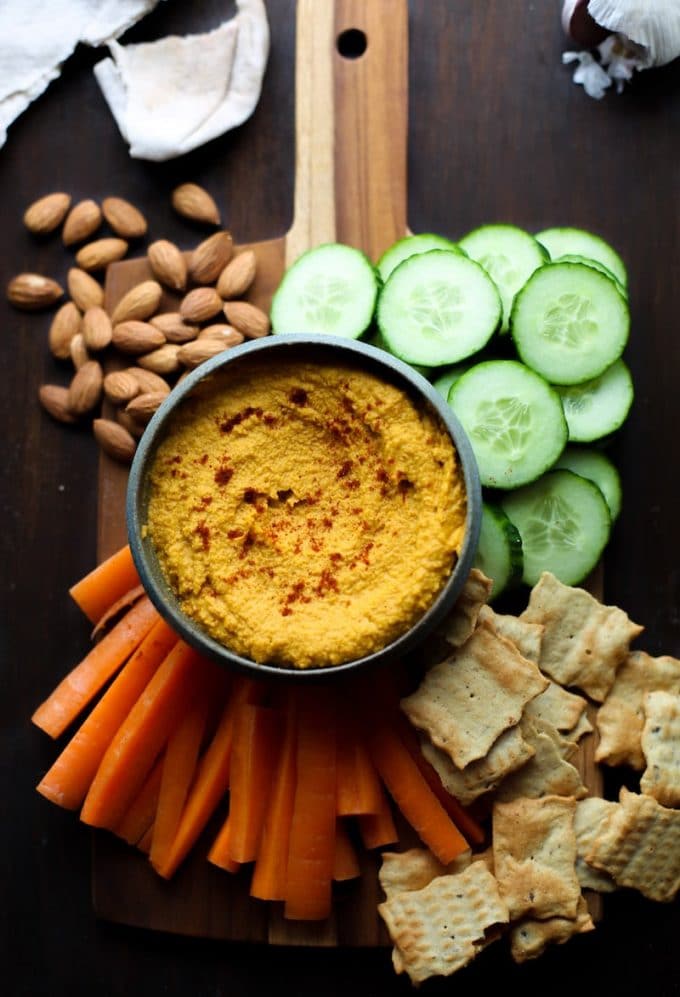 Roasted Carrot Hummus in a serving bowl on a platter with nuts and veggies