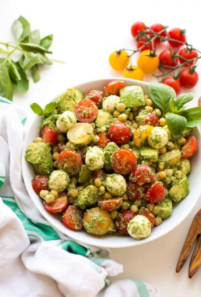 Avocado Chickpea Pesto Salad in a white bowl with tomatoes and fresh basil on the side