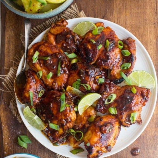 Honey Sriracha Chicken with a Pineapple Avocado Salsa on a plate topped with spring onions and lime slices