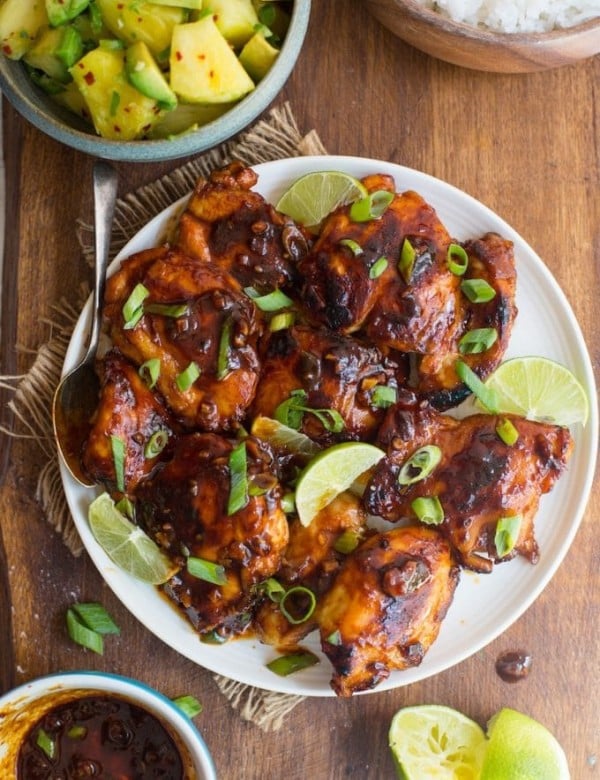 Honey Sriracha Chicken with a Pineapple Avocado Salsa on a plate topped with spring onions and lime slices