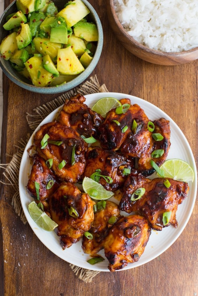 Honey Sriracha Chicken on a serving plate topped with sliced green onions and lime wedges