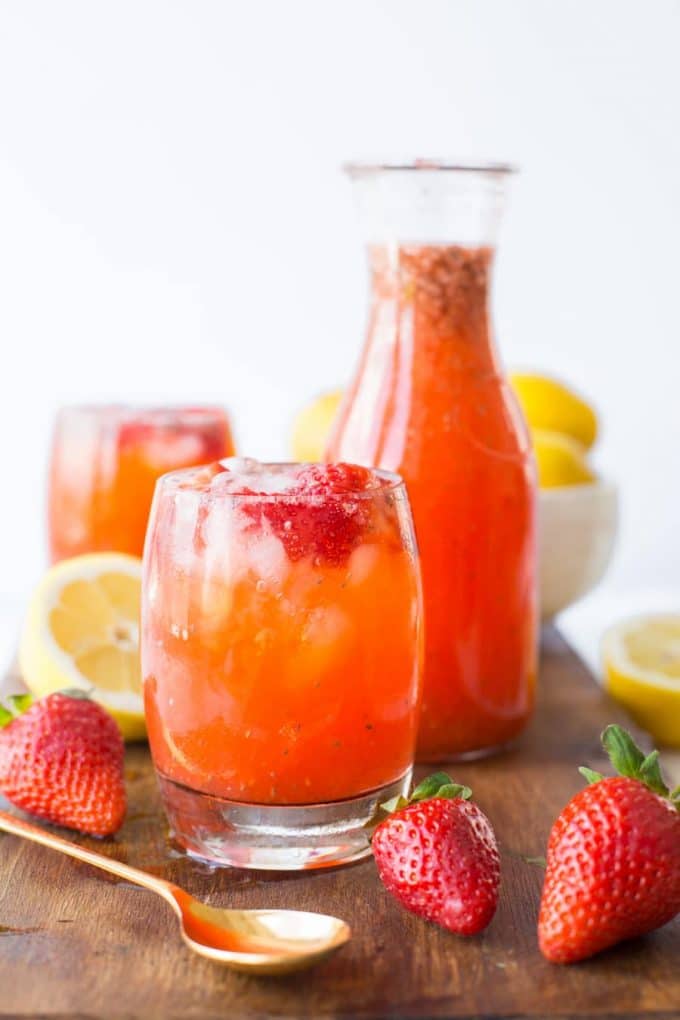  Strawberry Lemonade with chia seeds in a glass in front of a pitcher of lemonade
