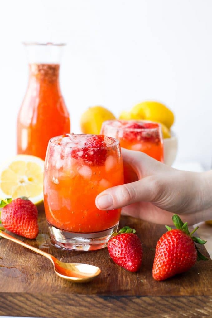 a hand pick up a glass of strawberry lemonade on a serving board with fresh berries