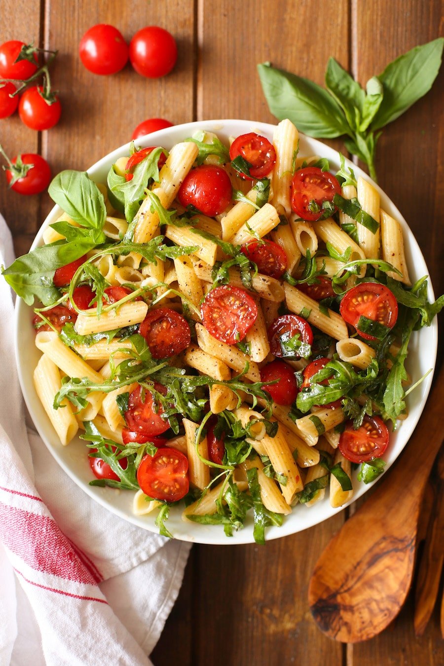 a big serving bowl full of Tomato & Arugula Balsamic Pasta Salad with whole cherry tomatoes and fresh basil on the side