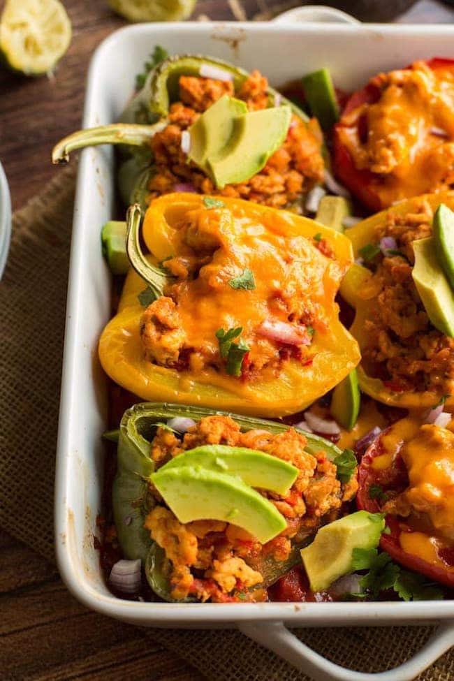 taco stuffed peppers - some topped with cheese and some topped with avocado 