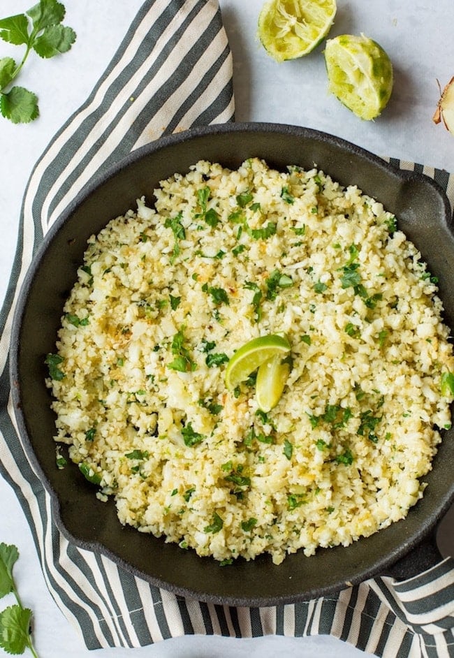 Cilantro Lime Cauliflower Rice topped with cilantro and limes in a cast iron skillet