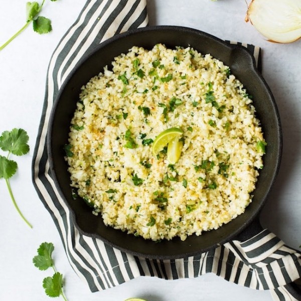 Cilantro Lime Cauliflower Rice in a cast iron skillet surrounded by limes and cilantro