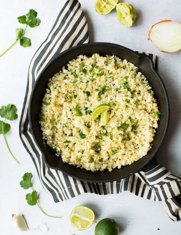 Cilantro Lime Cauliflower Rice in a cast iron skillet surrounded by limes and cilantro