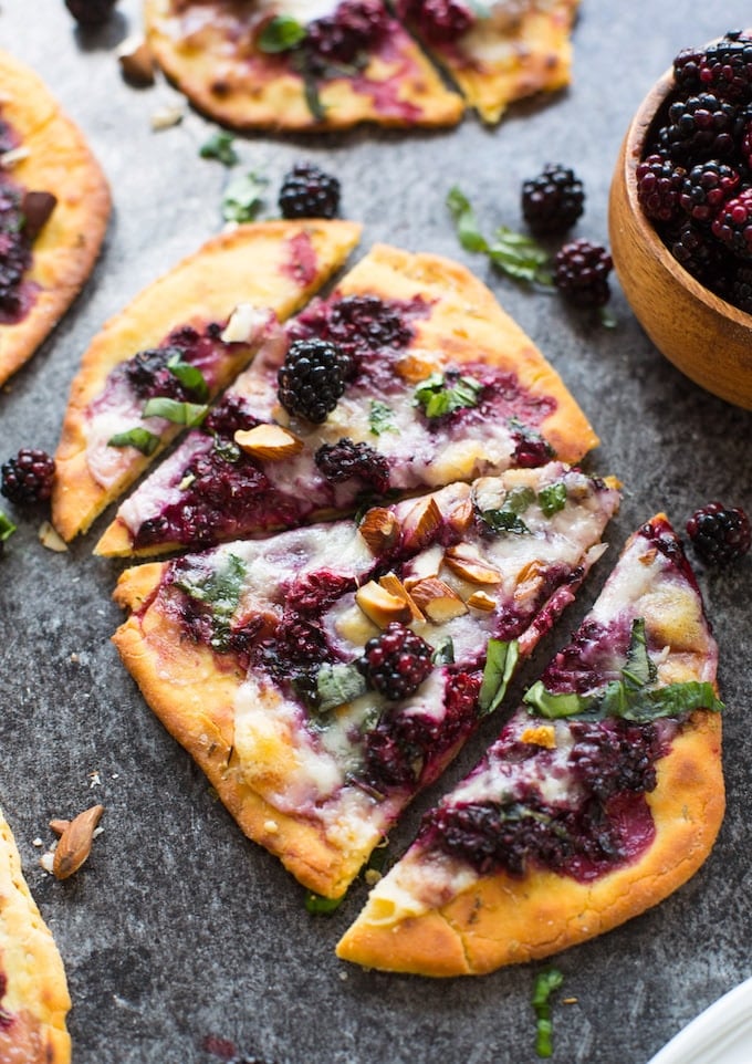 sliced blackberry flatbread pizzas on a granite background topped with basil and almonds